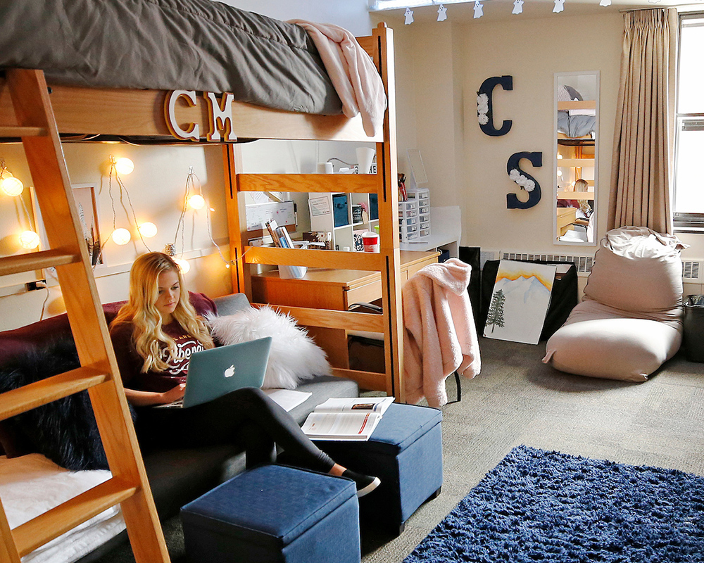Student sitting on couch below a lofted bed in her dorm room